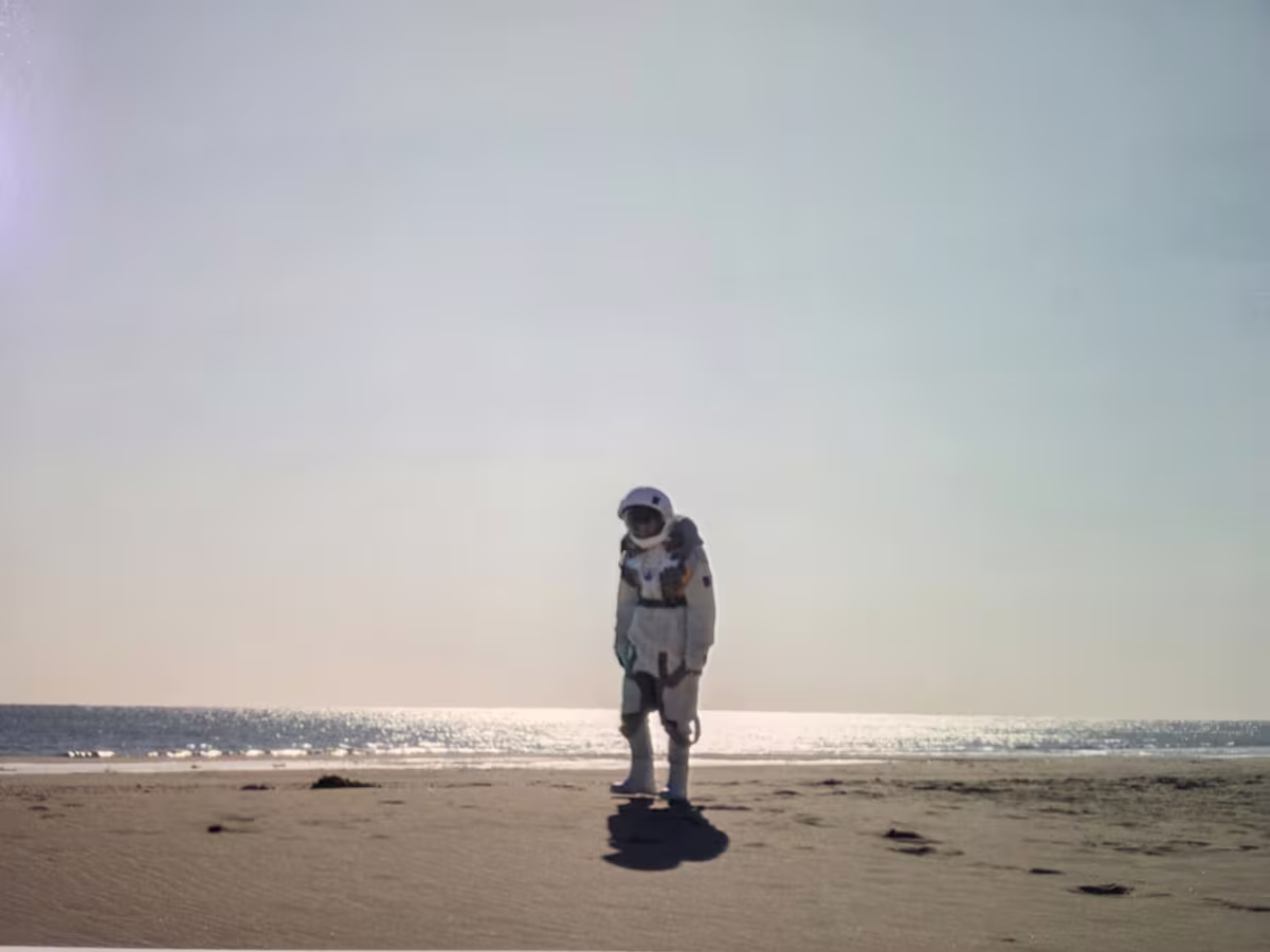 Videobild einer einzelnen Person im Raumanzug an einem Strand.