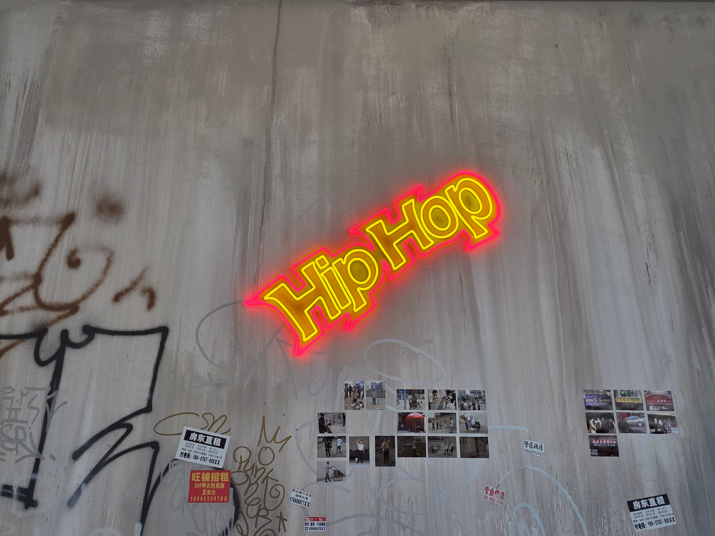 Ein Neonschriftzug «Hip Hop» an einer grauen Betonwand, darunter eine Reihe kleiner Dokumentarfotos.